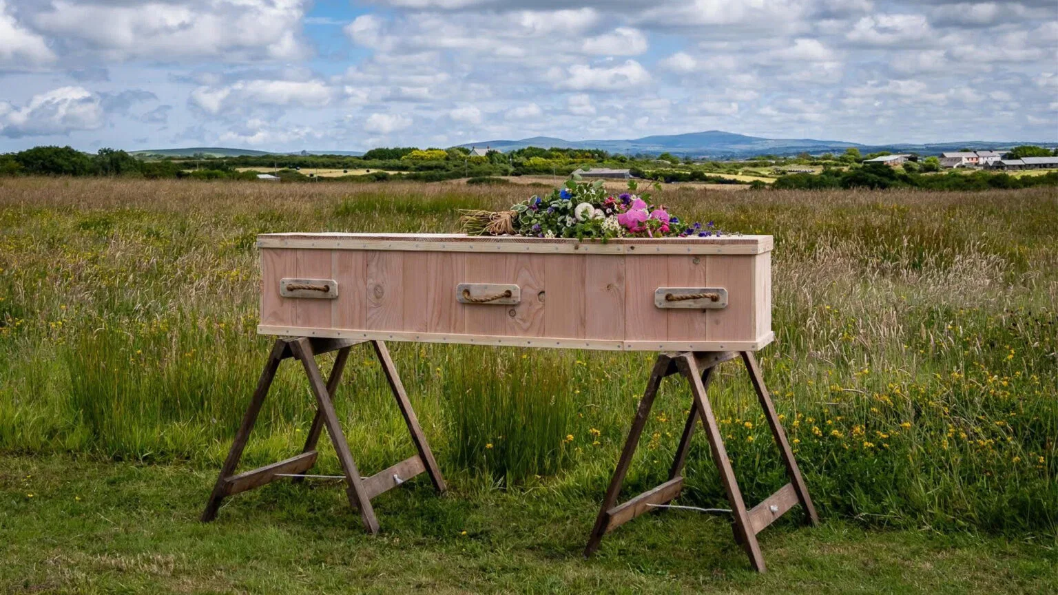 Houten kist met bloemen op schragen in een bloemrijke weide op natuurbegraafplaats Pembrokeshire