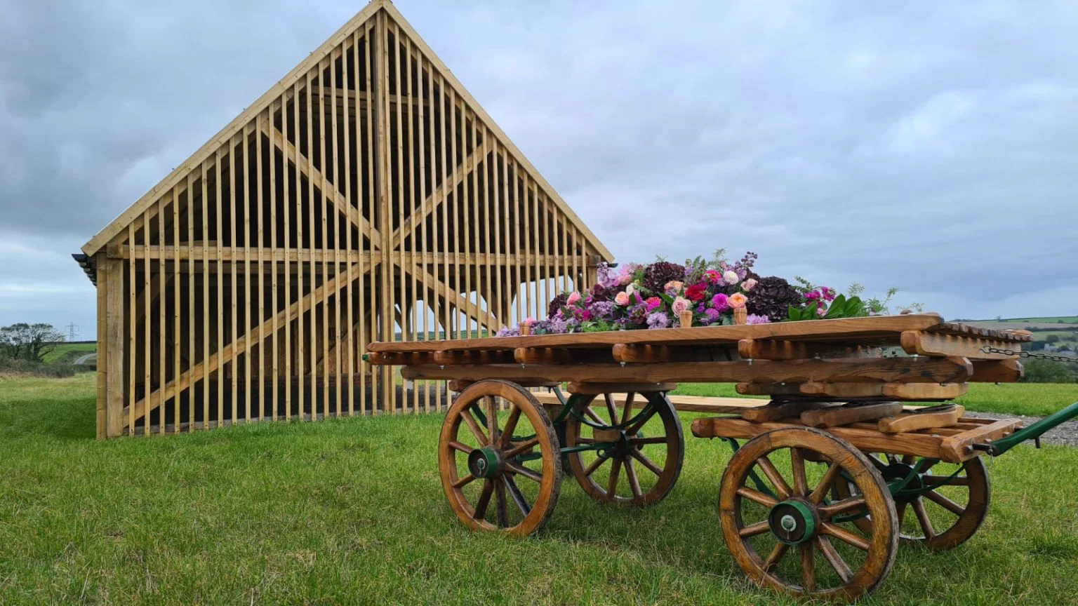 Open houten schuilhut met een bloemenkar in het gras op natuurbegraafplaats Dorset Downs