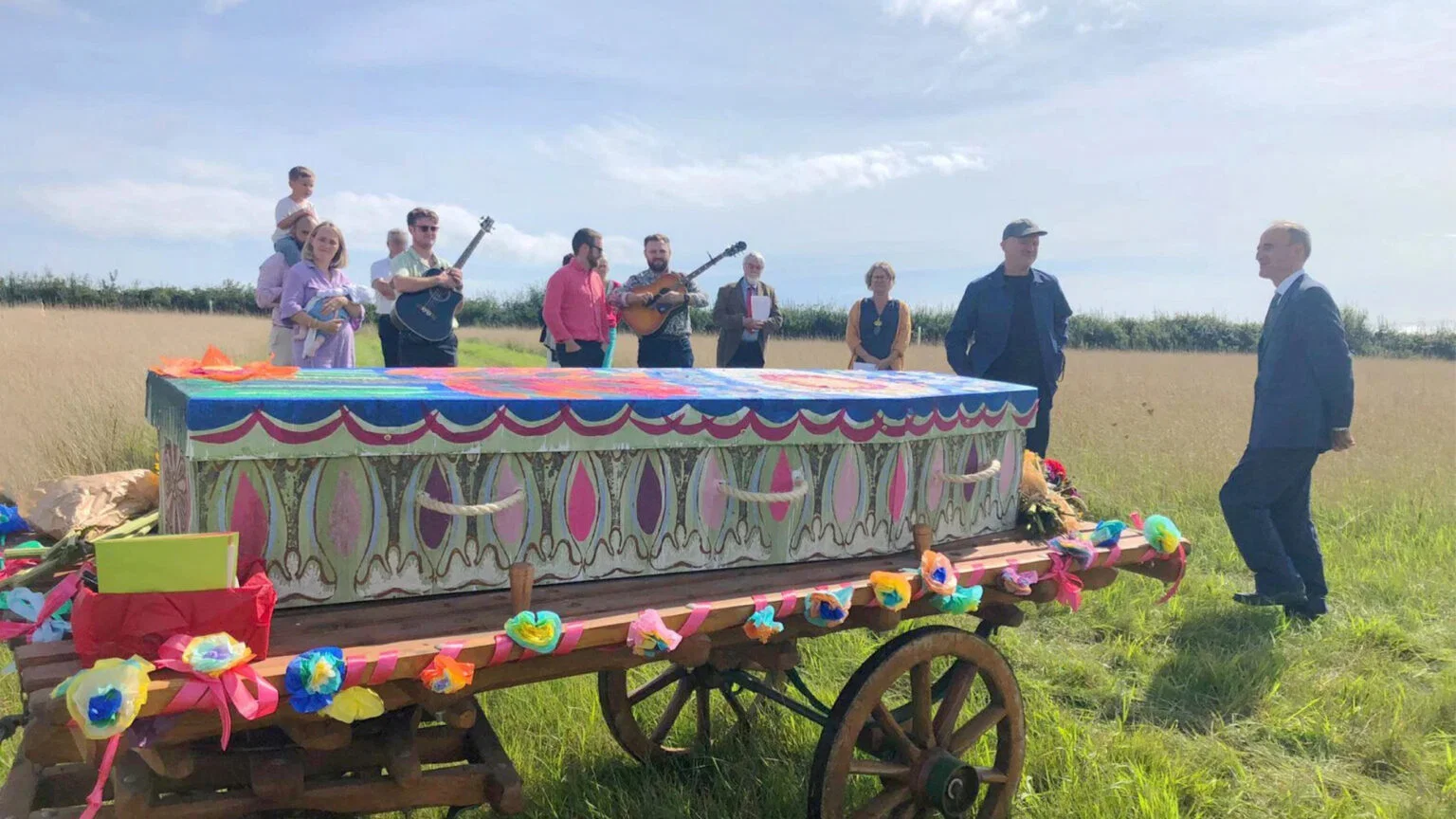 Gezelschap met muzikanten rond een beschilderde kist op een boerenkar in het veld