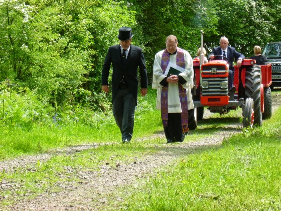 Uitvaartstoet met een tractor die de wagen met de kist over het land trekt