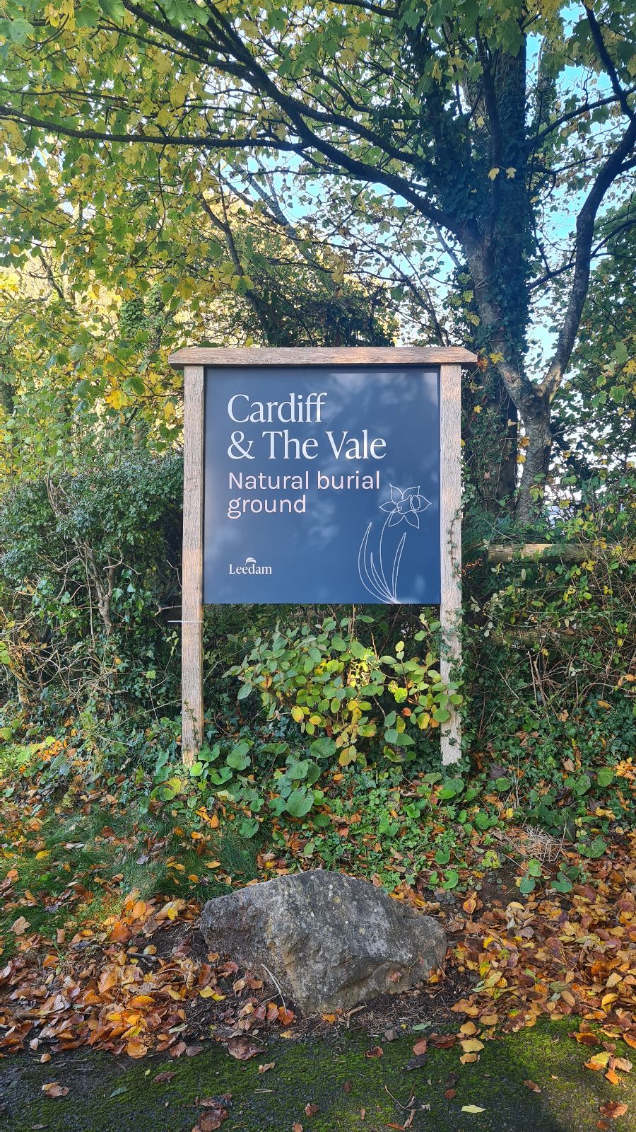 Houten bord van natuurbegraafplaats Cardiff & The Vale tussen groen en herfstblad