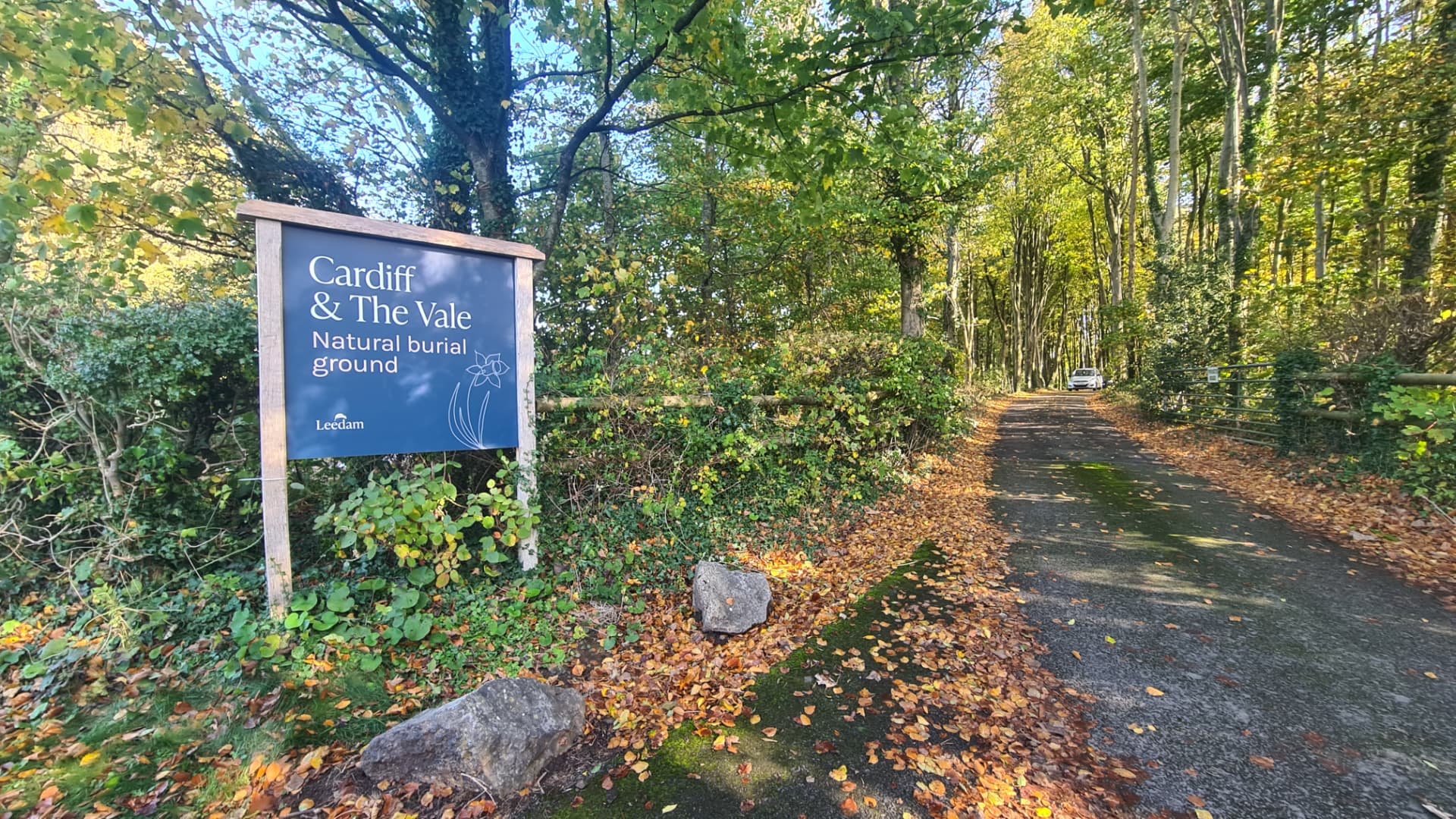 Entree van natuurbegraafplaats Cardiff met houten informatiebord aan een laan met volgroeide bomen