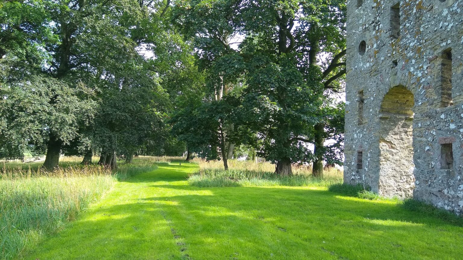Gemaaid graspad langs oude bomen naar de stenen folly van Hundy Mundy in de zomer