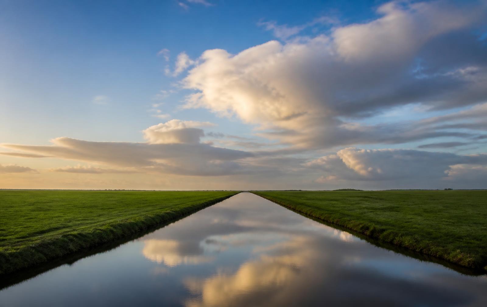Polderlandschap met rechte sloot en hoge wolkenlucht in avondlicht